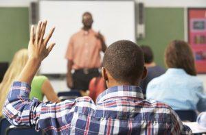 Black student in class with his hand raised.